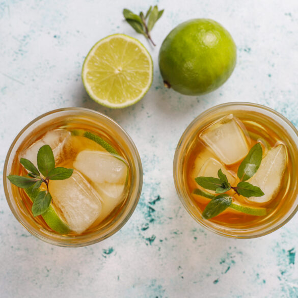 Iced tea with lime and ice on light background